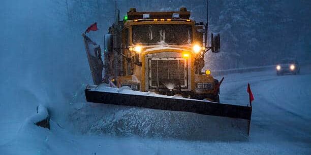 Truck plowing snow off the road at night.